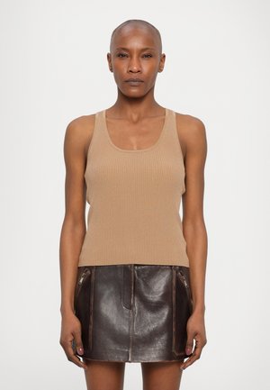 Débardeur côtelé de couleur beige associé à une mini-jupe en cuir marron dotée de zips et d'une texture lisse, mettant en valeur une silhouette ajustée.