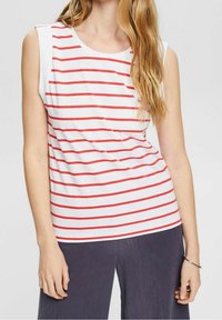 Top blanco sin mangas con rayas horizontales rojas, con un escote redondo y detalles en los hombros. Lleva pantalones anchos de pierna ancha oscuros y texturizados.