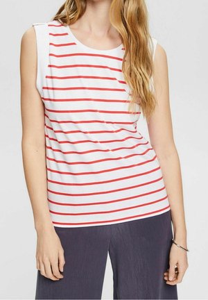 Top senza maniche bianco con righe orizzontali rosse, dotato di scollo tondo e dettagli sulle spalle. Indossato con pantaloni larghi scuri e testurizzati.