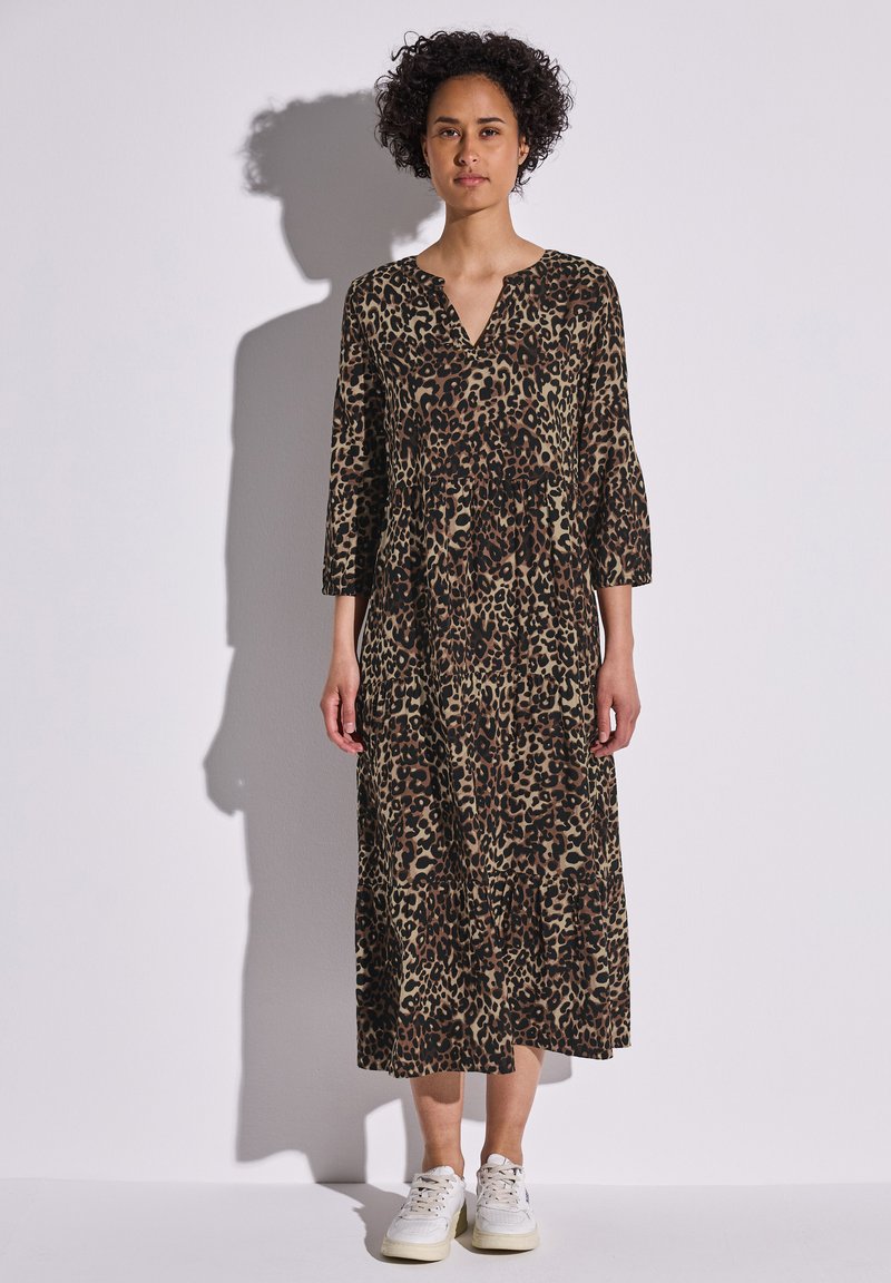 Vestido maxi de estampado de leopardo en tonos marrón y negro, con escote en V, mangas de tres cuartos y dobladillo en capas, combinado con zapatillas blancas.