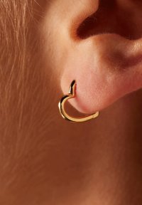 Gouden oorring in de vorm van een hart, met een gladde, gepolijste afwerking en een kleine, puntige accent aan de bovenkant.
