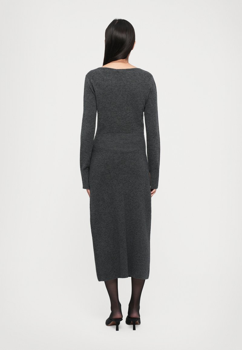 Langärmliges, dunkelgraues Strickkleid mit einer taillierten Taille, wadenlanger Länge und rundem Ausschnitt. Getragen mit schwarzen Absatzschuhen und transparenten Strumpfhosen.