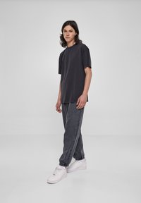 Tricou negru supradimensionat cu mâneci scurte, combinat cu pantaloni de tip jogger gri închis, cu manșete elastice și teniși albi.