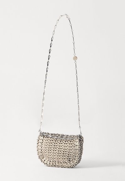 Bežs rokassomu ar teksturētu virsmu, kas ir ar metāla akcentiem un sudraba ķēdes siksnu. Apaļa forma ar izliekto augšu.