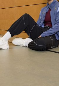 Marinblå zip-up jacka, vinröd topp, svarta joggers med vit sömnad, och vita sneakers med texturerade sulor och elastiska manschetter.