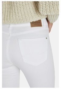 Jeans de mezclilla blanca con un bolsillo trasero y una etiqueta de cuero marrón que presenta "ANGELS" y "Denim Auténtico" en texto en relieve.