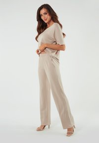 Beżowy zestaw odzieży domowej składający się z luźnej bluzki z krótkim rękawem oraz szerokich spodni z elastyczną talią, wykonany z miękkiego, gładkiego materiału.