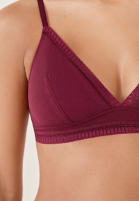 Bralette de couleur marron avec un design triangulaire, dotée de bretelles réglables, de bords texturés et d'une finition sans coutures.
