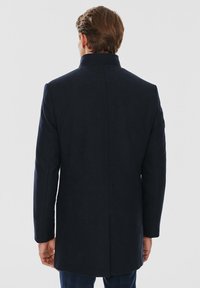 Navy niebieski płaszcz z wełny z prostym krojem, wysokim kołnierzem i długimi rękawami. Charakteryzuje się prostą, teksturowaną powierzchnią oraz detalami wentylacyjnymi z tyłu.