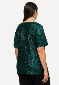 Top a maniche corte ricoperto di paillettes verdi, con una vestibilità morbida e un collo rotondo. Texture liscia con decorazioni lucide e riflettenti.