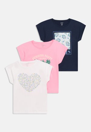 Τρία κοντομάνικα t-shirts σε λευκό, ροζ και ναυτικό μπλε με σχέδια με λουλουδάτη καρδιά, κείμενο καλοκαιρινού πάρτι και ελιά, στοιβαγμένα το ένα επάνω στο άλλο σε λευκό φόντο.