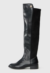 Stivale nero da donna fino al ginocchio con tacco basso, parte anteriore in pelle liscia, parte posteriore in suede e piccolo logo dorato "SM" vicino alla parte superiore.