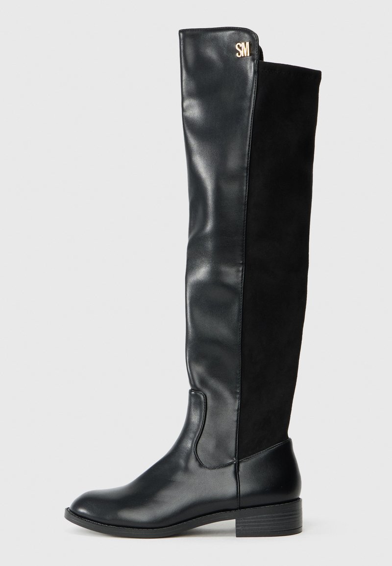 Stivale nero da donna fino al ginocchio con tacco basso, parte anteriore in pelle liscia, parte posteriore in suede e piccolo logo dorato "SM" vicino alla parte superiore.