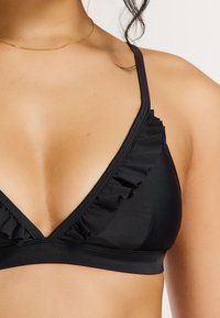 Juodas bikini viršus su giliais iškirpimais, raukšlėtomis detalėmis kraštuose, plonomis petnešėlėmis ir glotnia, elastinga audinio tekstūra.