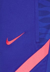 Blåt stof med et rødt Nike-swoosh-logo, en pink diagonal stribe og subtile mørkeblå abstrakte mønstre langs kanten.
