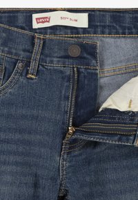 Levi's 511 Slim džiny v tmavomodrom denim sú vybavené zipsom, mosadzným zipsom a kontrastným žltým prešívaním na páse a vreckách.