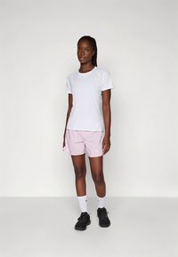 Bela športna majica s kratkimi rokavi v kombinaciji s svetlo roza kratkimi hlačami. Model nosi črne superge in bele nogavice. Preprost dizajn brez izrazitih vzorcev.