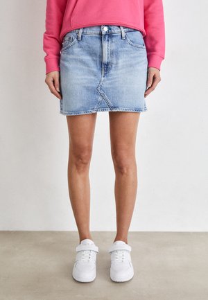 Gonna di jeans azzurro chiaro con una forma aderente, tasche frontali e orlo grezzo. Indossata con sneakers bianche e una felpa rosa.