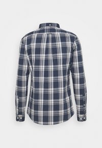 Chemise à manches longues boutonnée avec motif à carreaux bleu marine, blanc et gris, vue de dos.