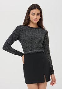 Maglione nero a maniche lunghe con un design testurizzato, caratterizzato da un collo rotondo e maniche aderenti, abbinato a una mini gonna nera con uno spacco laterale.