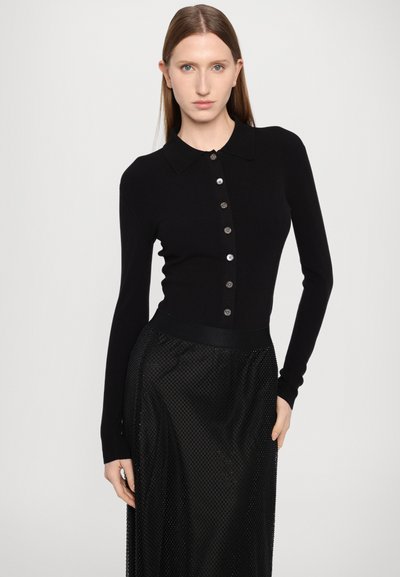 Cardigãs pretos com nervuras e um design justo, com gola e fecho frontal. Combinado com uma saia de rede preta translúcida.