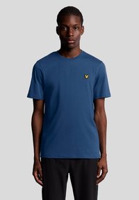 T-shirt in cotone blu con collo rotondo, maniche corte e logo giallo ricamato sul lato sinistro del petto. Texture liscia, vestibilità casual.