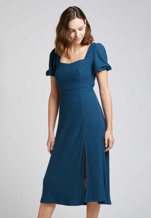 Robe bleue texturée avec des manches bouffantes, décolleté carré et fente sur le côté, présentant un corsage ajusté et une jupe fluide, en tissu extensible.