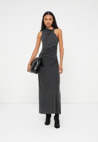 Bez rukava, tamno siva haljina s naborima, do koljena, glatka tkanina, uparena s crnom torbicom i cipelama s potpeticama.