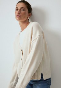 Cr�ème-kleurige cardigan met een V-hals, knoopsluiting, ingezakte schouders, geribbelde manchetten en zoom. Draagt over een witte top en denim.