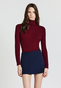 Burgunderfarbener, gestrickter Rollkragenpullover mit geripptem Muster, kombiniert mit einem enganliegenden, marineblauen Minirock. Schlichtes Design und einfarbige Ausführung.