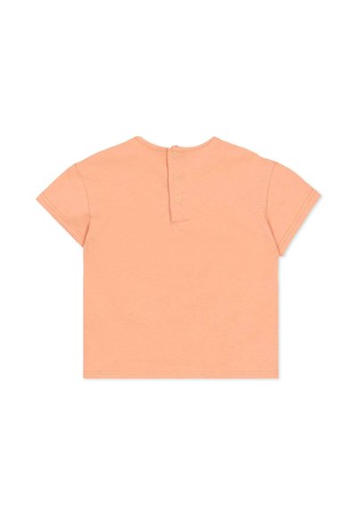 Brzoskwiniowa koszulka niemowlęca z krótkim rękawem, zapinana z tyłu na trzy napy, z okrągłym dekoltem, rozłożona płasko na białym tle.