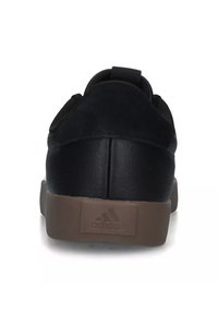 Zapatillas negras con parte superior de ante texturizado, paneles laterales elásticos y suela de goma marrón con detalle de logo grabado en el talón.