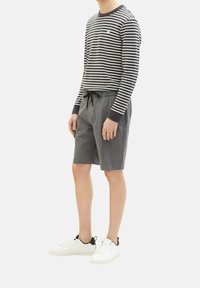 Camicia a maniche lunghe a righe in blu navy e bianco, abbinata a pantaloni corti grigi con cordino. Sneakers bianche con dettagli neri.