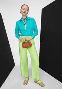 Camisa de botones turquesa con pliegues, combinada con pantalones de pierna ancha color lima brillante, minibolso marrón y chanclas verdes con acentos de lazo.