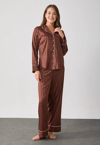 Σετ καφέ σατέν πιτζάμες με κάθετες ρίγες, πουκάμισο με γιακά και κούμπωμα με κουμπιά, μακριά μανίκια και παντελόνι που ταιριάζει με λευκά διακοσμητικά κορδόνια.
