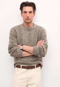 Tekstūrēta brūna adīta džemperis ar apaļu kakla izgriezumu, salikts ar krējuma krāsas biksēm un brūnu jostu. Iespējas sudraba rokas pulkstenis.