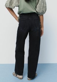 Jeans de mezclilla negros de cintura alta con un corte relajado, que cuentan con dos bolsillos traseros y detalles de costura mínimos para un aspecto limpio.