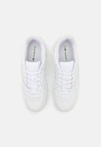 Hvite snøresko i lakket skinn med perforert design. Laget av glatt lær, med en grønn Lacoste-logo på sålen og sømadetaljer.