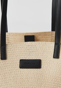Borsa a rete in paglia di colore naturale con manici in pelle nera e un'etichetta nera con la scritta "OPUS". Design testurizzato e aperto.