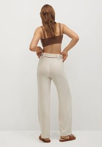 Un crop top en tricot marron associé à un pantalon large beige, doté d'une taille ceinturée. Le tissu semble doux avec une texture lisse.