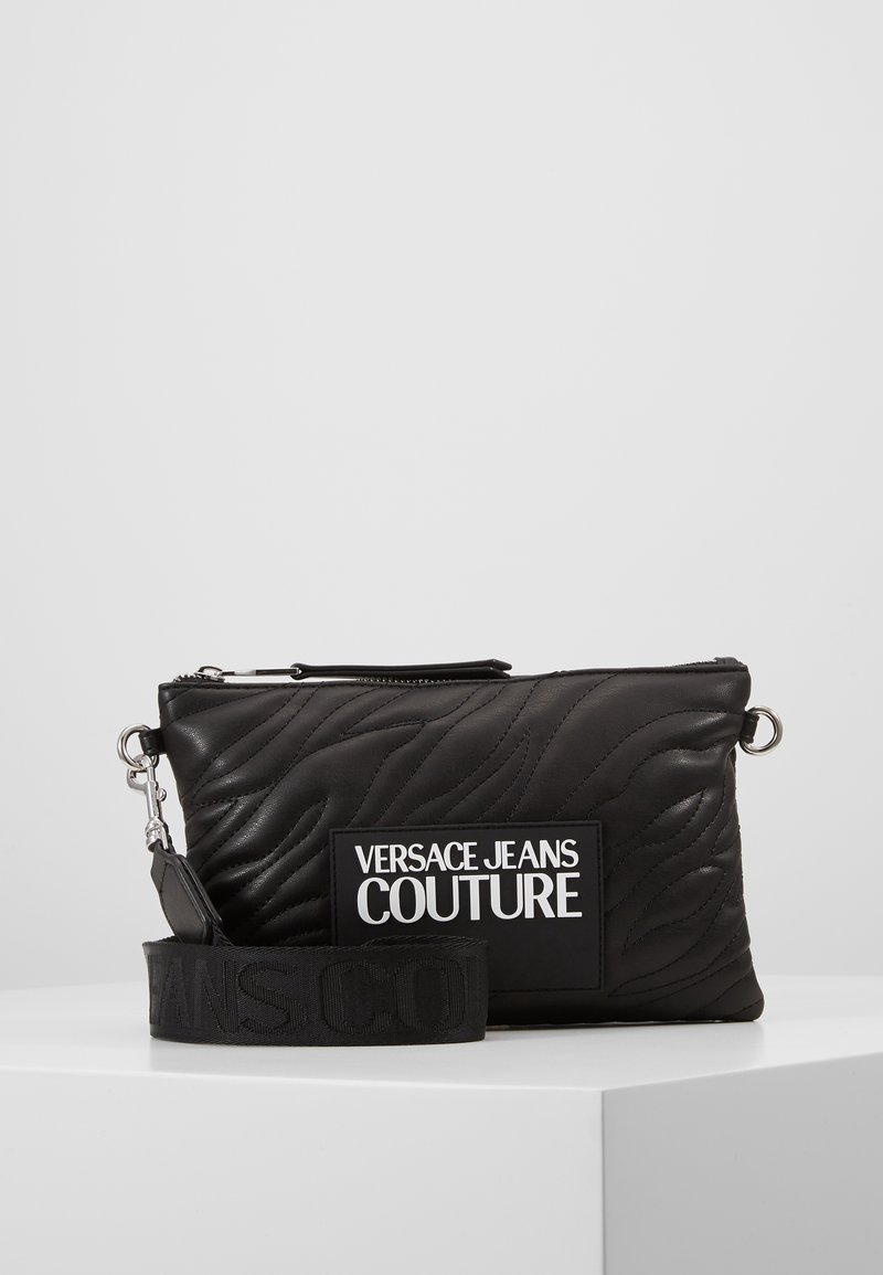 Svart kviltad läderclutch med en stor logopatch, metalliska accenter och ett avtagbart band med präglad text.