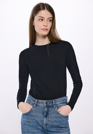 Zwarte lange mouwen shirt met een ronde halslijn, gecombineerd met lichtblauwe hoge taille jeans. De stof lijkt glad en aangesloten.