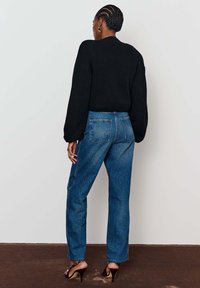 Juodas megztinis su ilgomis rankovėmis, derinamas su mėlynomis džinsinėmis kelnėmis, turinčiomis klasikinį penkių kišenių dizainą. Lygus audinys ir laisvas siluetas.