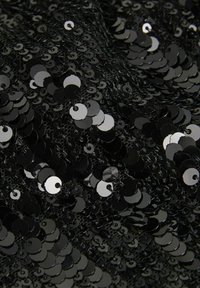 Tessuto di paillettes nere con paillettes circolari che riflettono la luce, creando una superficie tessurizzata. L'arrangiamento è denso e uniformemente circolare.