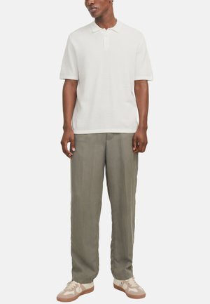 Polo shirt bianco con texture e maniche corte, abbinato a pantaloni grigi chiari larghi e sneaker beige con motivi chiari.