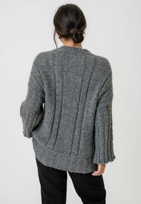 Maglione grigio lavorato a maglia con un design a coste testurizzato. Presenta una vestibilità ampia e morbida e maniche leggermente svasate. Filato morbido e spesso.