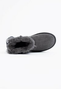 Botín de ante gris con un forro de piel de peluche y textura suave. Punta redondeada y suela plana, con un acento estampado en la parte superior.