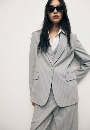 Light gray pinstripe suit with blazer and trousers. Smooth fabric, single-button closure, and two front pockets. White shirt underneath.
