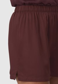 Shorts sportivi bordeaux con vita elasticizzata, aperture laterali all'orlo e una texture liscia, adatti per l'abbigliamento attivo.