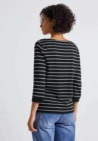 Zwart-wit gestreepte lange mouw top met een brede halslijn, losse pasvorm en ribgebreide manchetten, gecombineerd met blauwe denim.